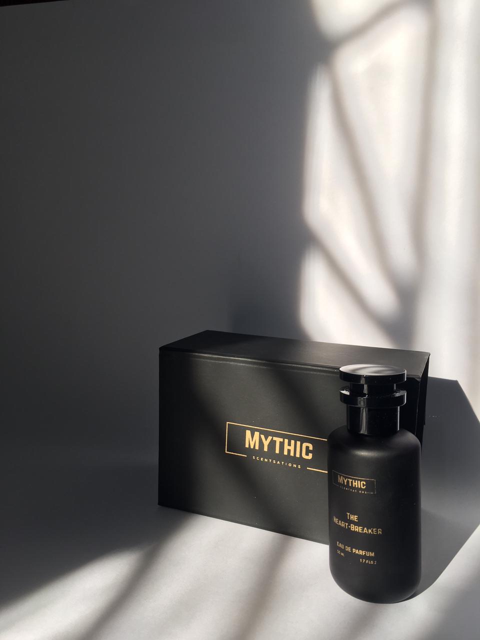 Black 'MYTHIC' perfume bottle and packaging on a dark surface with light shadows.