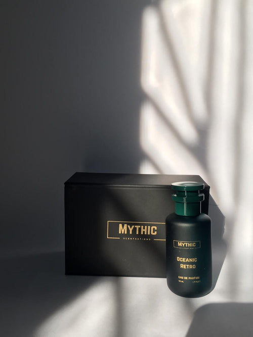 Black 'Mythic' perfume bottle and packaging on a gray surface with light shadows.