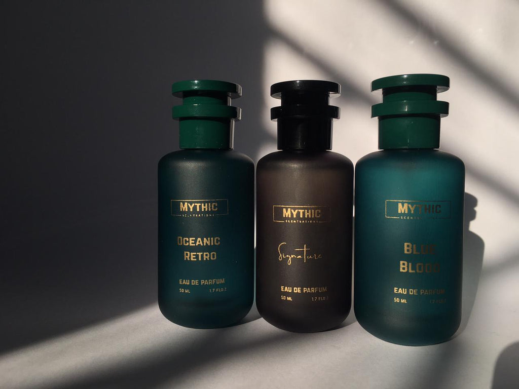 Three bottles of Mythic perfume on a reflective surface with a dark background
