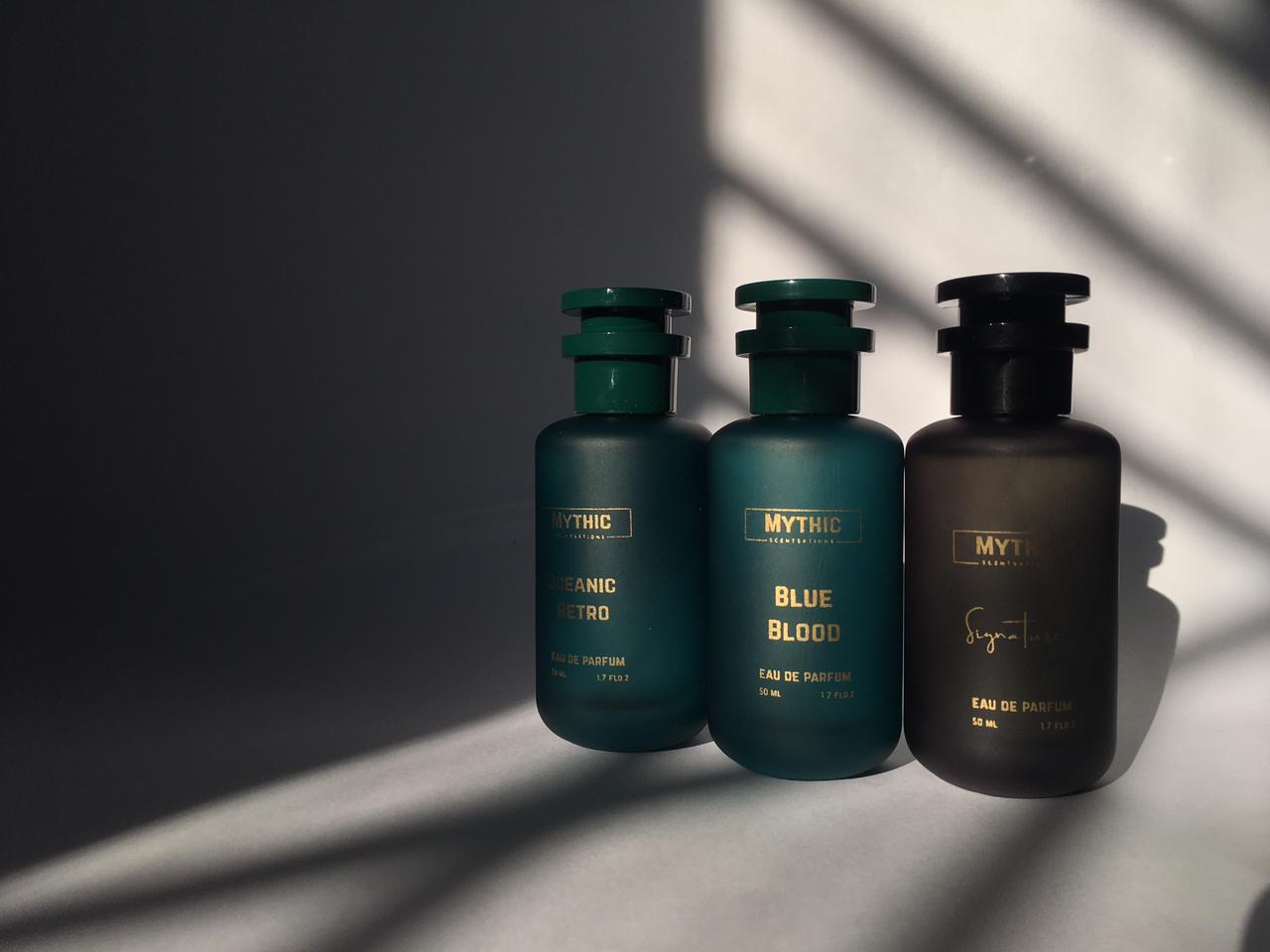 Three bottles of Mythic perfume on a reflective surface with shadows cast by sunlight.